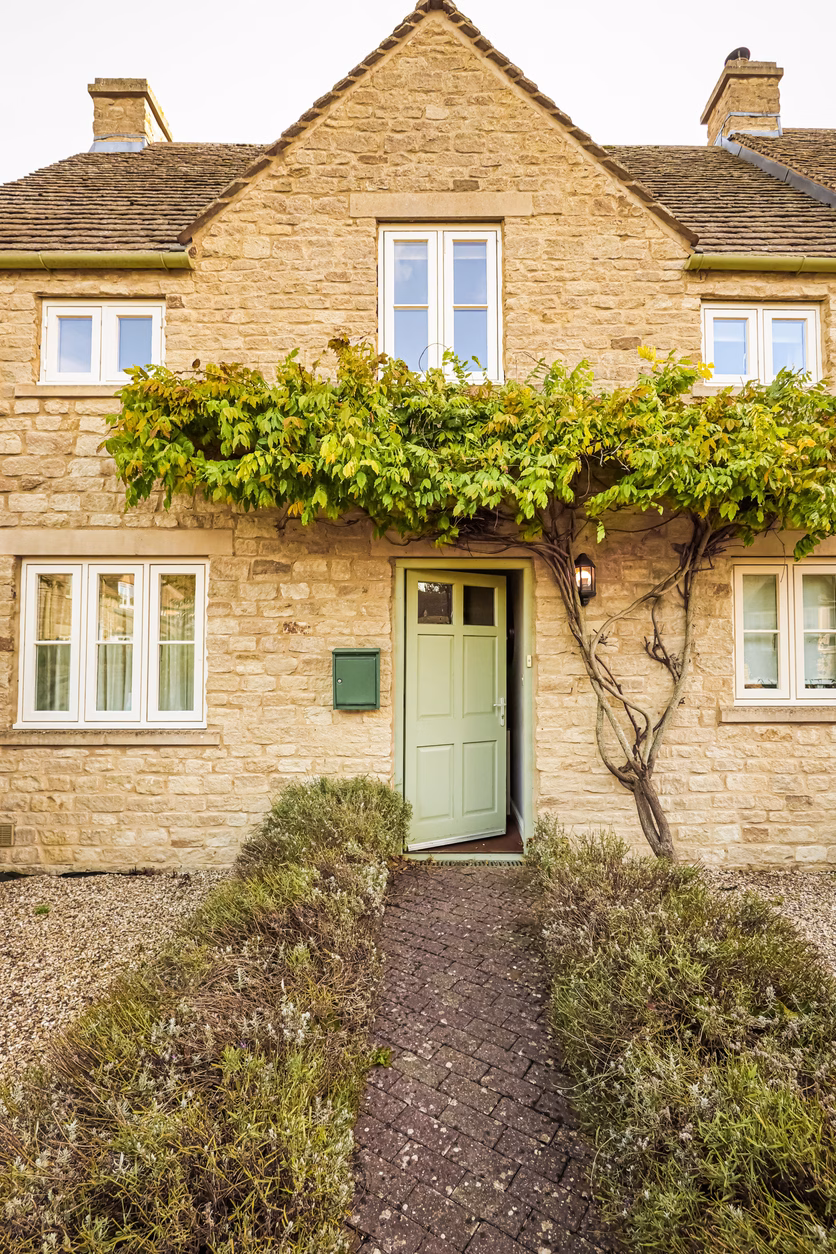 Cotswold stone cottage with open door and lush wisteria vine, welcoming home. Cotswolds countryside, England